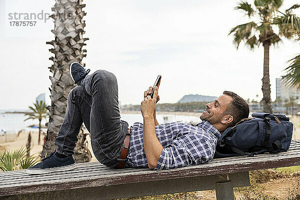 Lächelnder reifer Mann entspannt sich mit Smartphone auf Bank