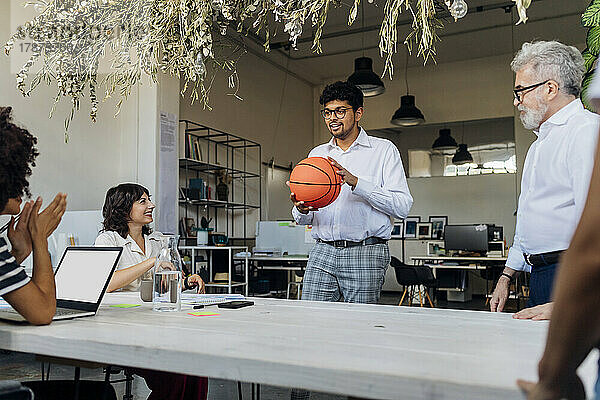 Geschäftsmann hält Basketball und unterhält sich mit Kollegen im Büro