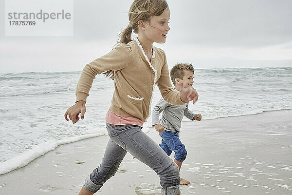 Brother and sister having fun running on the beach