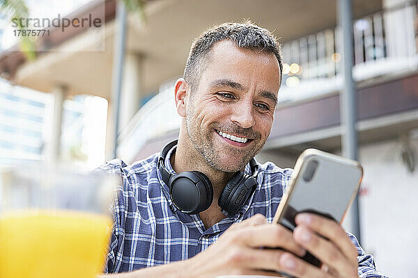 Glücklicher reifer Mann  der im Straßencafé sein Mobiltelefon benutzt