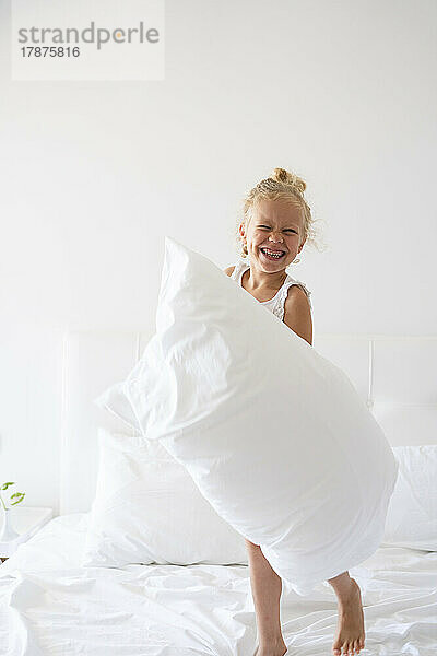 Glückliches Mädchen mit Kissen  das Spaß auf dem Bett hat