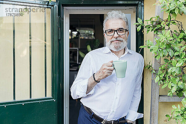 Älterer Geschäftsmann mit Kaffeetasse lehnt an der Tür
