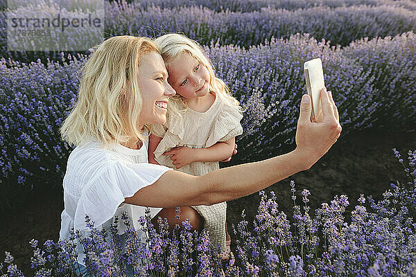 Glückliche Frau macht ein Selfie mit ihrer Tochter über ihr Smartphone inmitten von Lavendelblüten