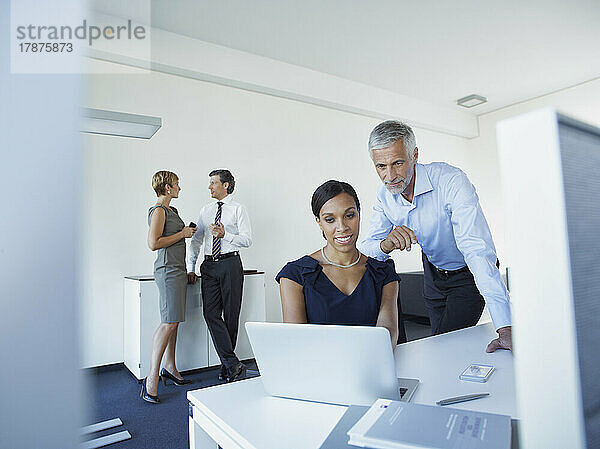 Reifer Geschäftsmann und Geschäftsfrau nutzen Laptop mit Kollegen und diskutieren im Büro