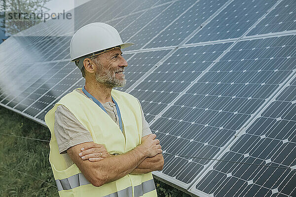 Lächelnder Ingenieur mit verschränkten Armen und Blick auf Solarpanel