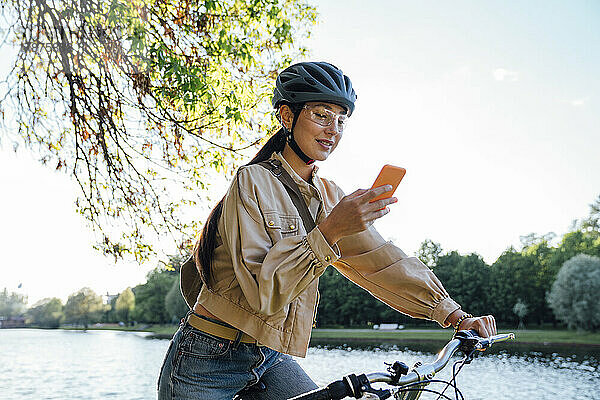 Frau auf dem Fahrrad benutzt Mobiltelefon im Park