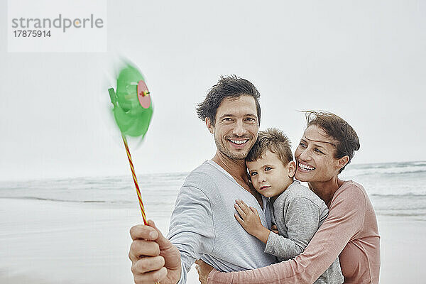 Glückliche Familie steht am windigen Strand und hält ein grünes Oinwheel in der Hand