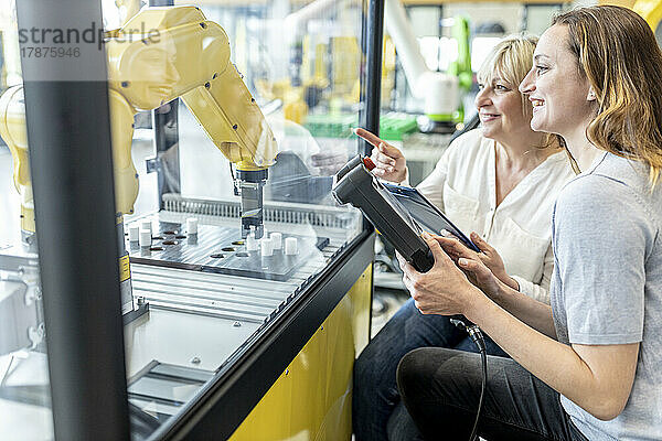 Frauen in der Fabrik nutzen die Steuerung eines Industrieroboters