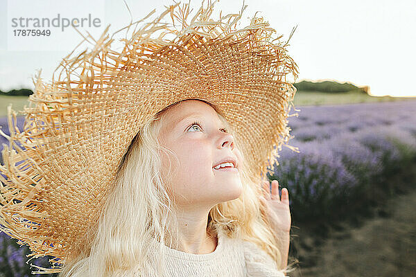 Lächelndes süßes Mädchen mit Hut  das im Lavendelfeld steht