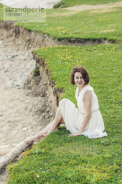 Lächelnde Frau in weißem Kleid sitzt auf Gras