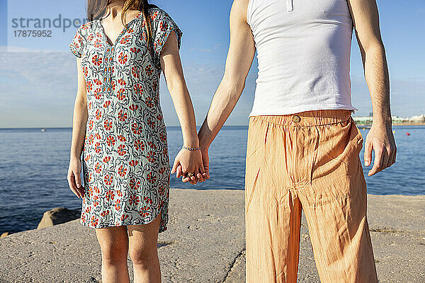 Couple holding hands at pier on sunny day