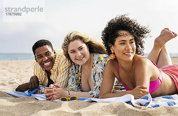 Fröhliche gemischtrassige Freunde  die am Strand auf einem Handtuch liegen