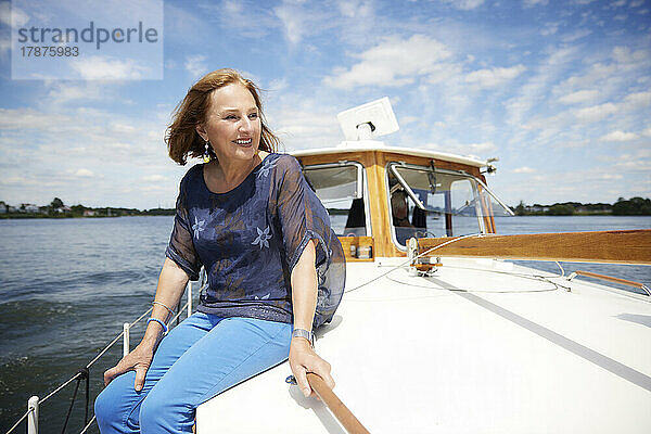 Glückliche ältere Frau  die im Urlaub auf dem Bootsdeck sitzt