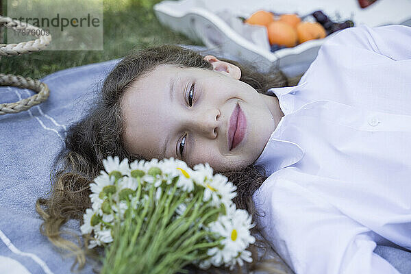 Lächelndes Mädchen  das Kamillenblüten betrachtet  die im Park liegen