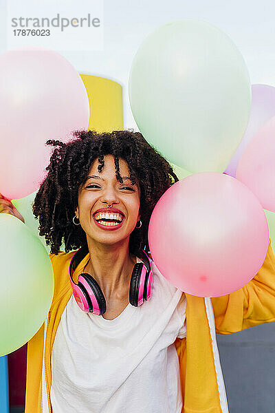 Fröhliche Frau mit lockigem Haar  die bunte Luftballons hält
