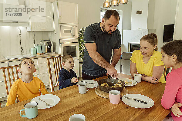 Vater serviert Frau und Kindern zu Hause Frühstück