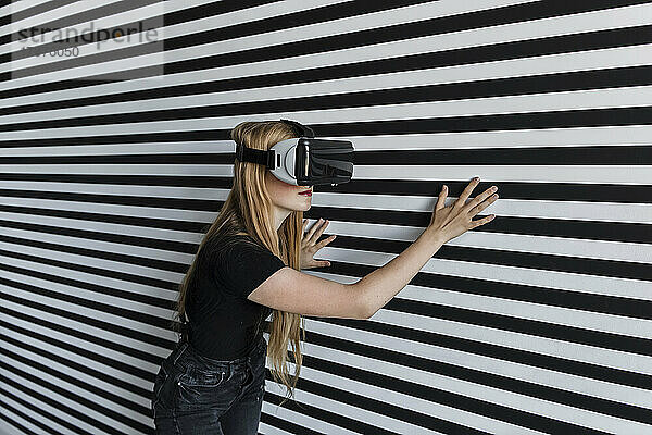 Mädchen mit Virtual-Reality-Headset berührt gestreifte Wand
