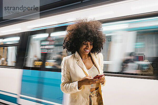 Lächelnde Frau benutzt Smartphone vor fahrender U-Bahn