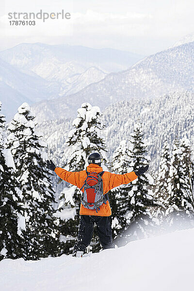 Mann steht mit ausgestreckten Armen vor schneebedecktem Wald
