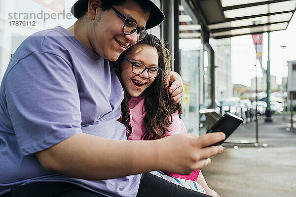 Lächelnder Bruder teilt Smartphone mit Schwester am Busbahnhof