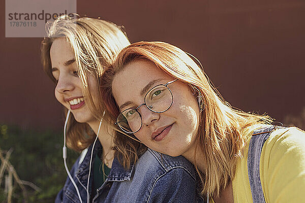 Young woman by friend listening music through in-ear headphones