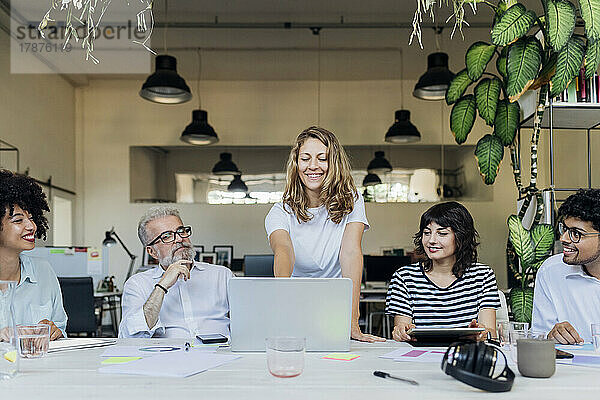 Lächelnde Geschäftsfrau plant Strategie am Laptop mit Kollegen im Büro