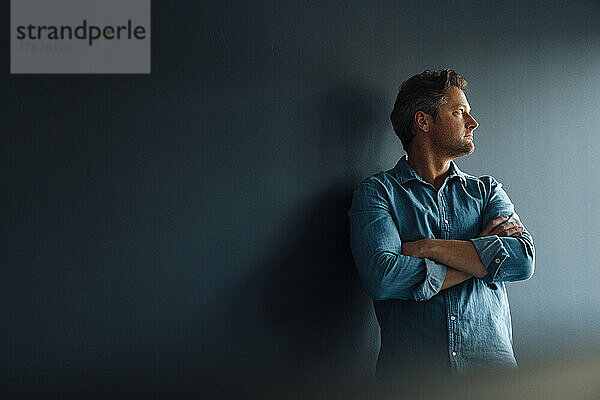 Thoughtful mature businessman standing in front of wall