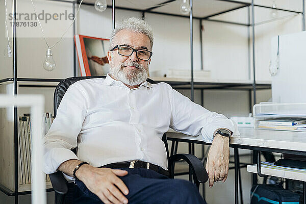 Leitender Geschäftsmann mit Brille sitzt auf einem Stuhl im Büro