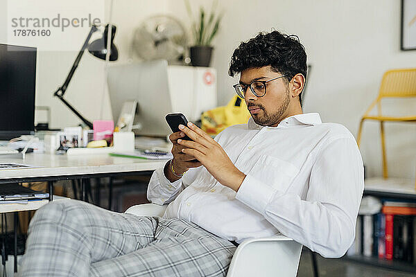 Junger Geschäftsmann sitzt am Arbeitsplatz und nutzt sein Smartphone