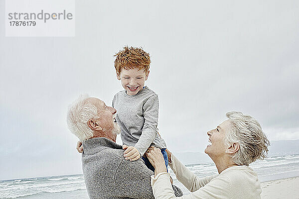 Fürsorgliche Großeltern umarmen ihren Enkel am Strand