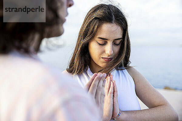 Young woman meditating with hands clasped by boyfriend