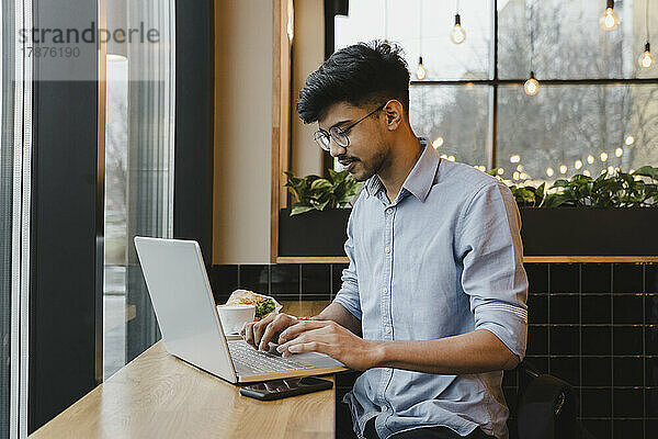 Junger Freiberufler arbeitet am Laptop im Café