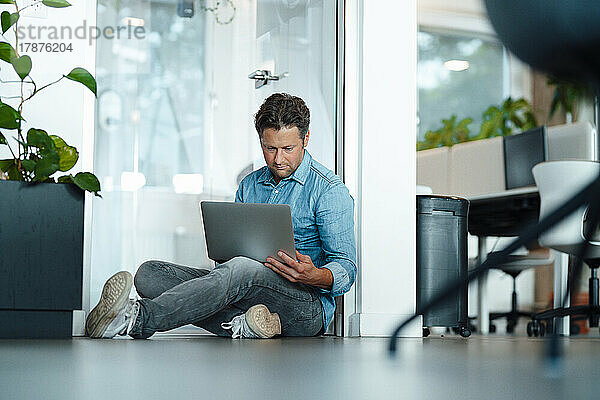 Geschäftsmann sitzt mit Laptop auf dem Boden im Büro