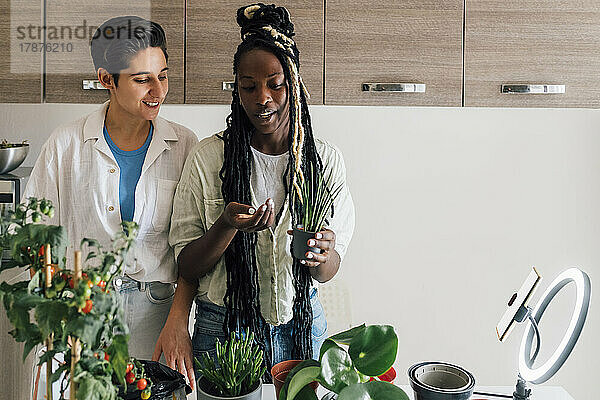 Lächelnde junge Frau mit Freundin filmt zu Hause Tutorial zur Pflanzenpflege