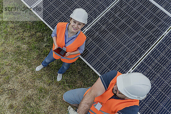 Glückliche Frau mit Tablet-PC steht neben Kollege am Solarpanel