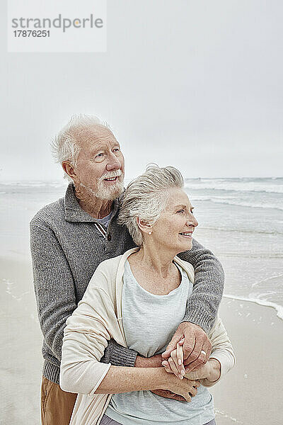 Glückliches älteres Paar  das lächelnd am windigen Strand steht