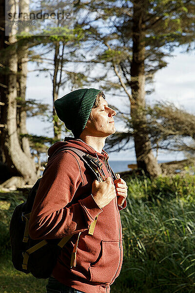 Mann mit Rucksack genießt Sonnenlicht im Wald