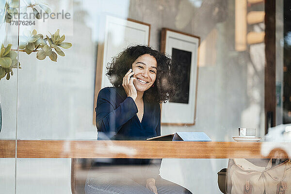 Glückliche Frau  die am Tisch im Café mit dem Smartphone spricht