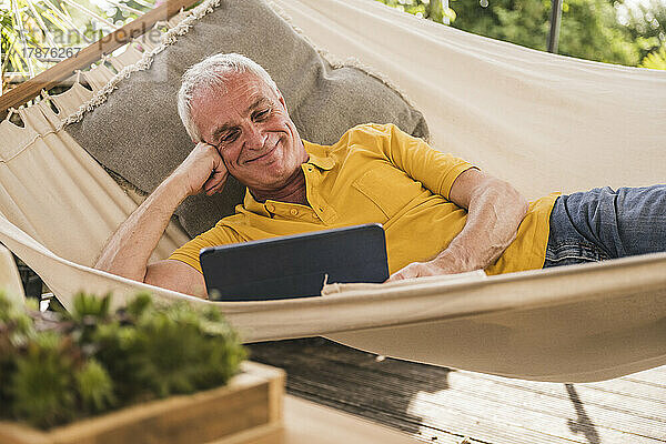 Smiling man using tablet PC lying in hammock