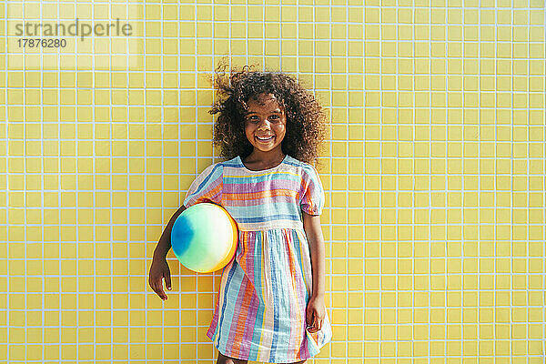 Nettes Mädchen mit Wasserball an einem sonnigen Tag  das vor der Wand steht