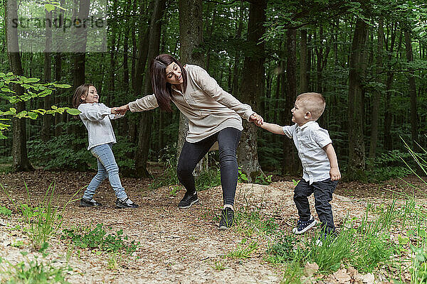 Glückliche Kinder ziehen Mutter und haben Spaß im Wald