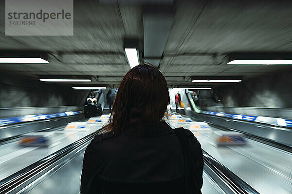 Young woman standing on escalator moving down