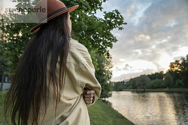 Frau mit Hut blickt auf den Sonnenuntergang im Park