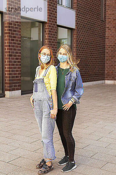 Junge Freunde tragen eine schützende Gesichtsmaske auf dem Fußweg