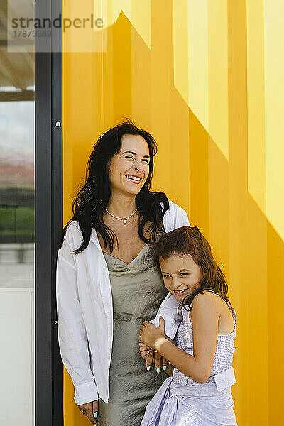Happy mother and daughter standing in front of yellow wall