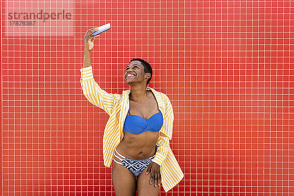 Fröhliche Frau im Bikini macht ein Selfie mit dem Handy