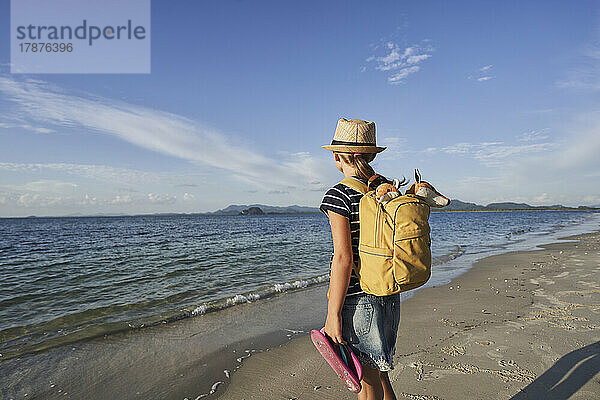 Mädchen mit Rucksack steht an einem sonnigen Tag am Meer