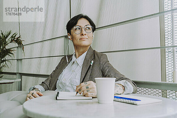 Geschäftsfrau mit Brille sitzt mit Tagebuch und Einwegbecher im Café