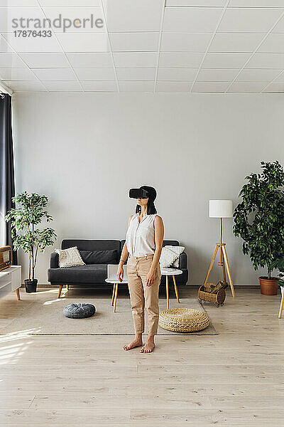 Frau mit Virtual-Reality-Simulatorbrille steht im Wohnzimmer
