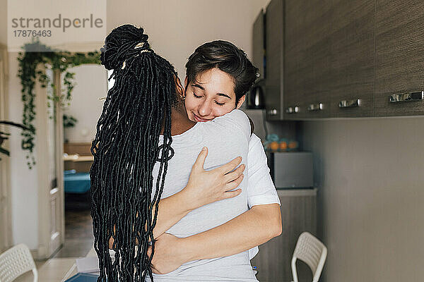 Smiling woman with eyes closed embracing girlfriend at home